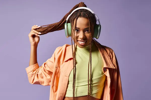 stock image happy african american young woman in headphones holding her dreadlocks on purple background