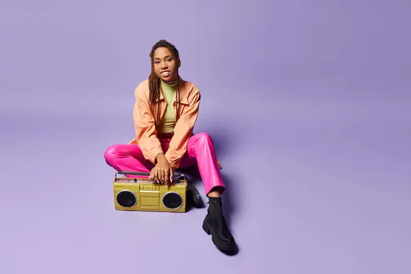 紫色の背景にレトロブームボックスの隣に座っているドレッドロックを持つ陽気なアフリカ系アメリカ人女性 — ストック写真
