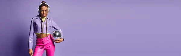 トレンディな服装とヘッドフォンで若いアフリカ系アメリカ人女性 紫のディスコボールを保持 バナー — ストック写真