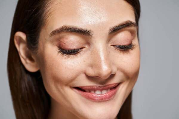 A young Caucasian woman with brunette hair smiles serenely, eyes closed in a moment of pure happiness.