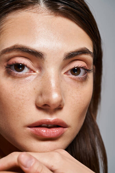 A close-up of a young Caucasian woman with mesmerizing brown eyes and flawless skin in a studio setting.