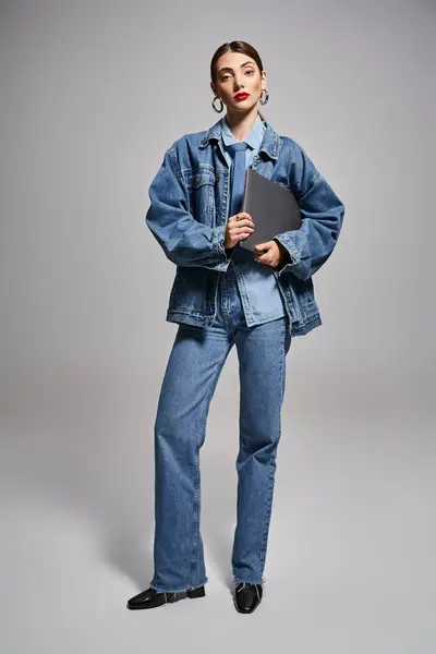 一位白种人的年轻女子 一头乌黑的头发 自信地穿着牛仔夹克和牛仔裤 手持笔记本电脑 — 图库照片