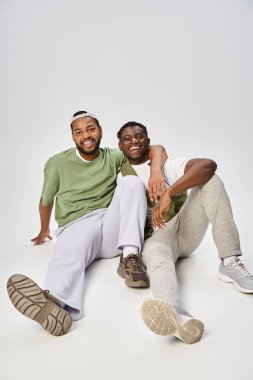 happy Juneteenth celebration, excited and young african american mates hugging on grey background clipart