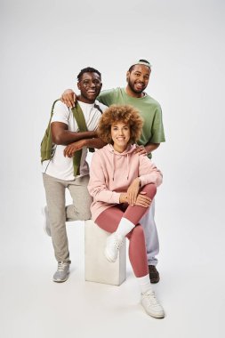 Neşeli Afro-Amerikan erkekleri gri arka planda kıvırcık bir kadının yanında poz veriyorlar, Haziran kutlamaları.
