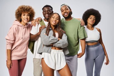 Mutlu Afro-Amerikalı kadın spor kıyafetleri içinde arkadaşlarının yanında poz veriyor gri arka planda, Juneteenth