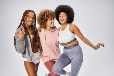 Mutlu Afro-Amerikan dostları spor kıyafetleri içinde gri zeminde poz veriyorlar, Haziran kutlamaları.