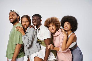 Bir grup pozitif genç Afrikalı Amerikalı, gri arka planda birbirlerine yaslanıyorlar.
