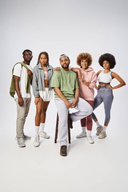 Bir grup iyimser genç Afrikalı Amerikalı arkadaş gri arka planda, toplumda bir arada duruyorlar.