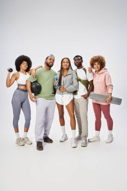 Sportif genç Afrikalı Amerikalı arkadaşlar gri arka planda spor malzemeleriyle duruyorlar.