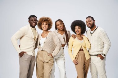 Gri arka planda elleri ceplerinde poz veren bir grup mutlu Afrikalı Amerikalı erkek ve kadın.