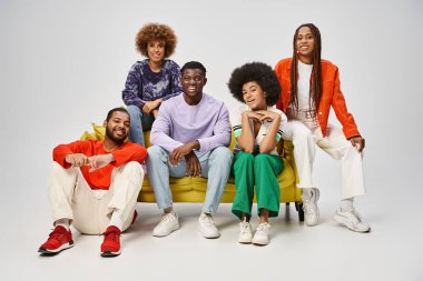 Neşeli Afro-Amerikan halkı günlük kıyafetlerini giyer ve gri koltukta otururlar.