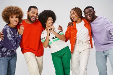 Mutlu Afro-Amerikan insanları gri arka planda birlikte gülerek günlük kıyafetlerini giyerler.