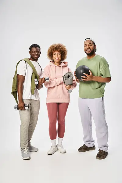 stock image happy african american friends holding yoga mat, ball and dumbbells on grey background, wellness