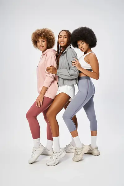 stock image joyful african american female friends in sportswear standing together on grey backdrop, Juneteenth