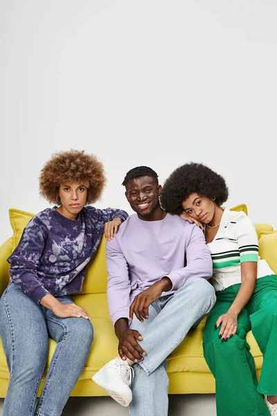 young and curly african american friends together sitting on yellow sofa on grey background, comfort