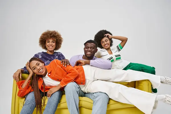 excited african american woman with dreadlocks lying on laps of friends sitting on yellow couch