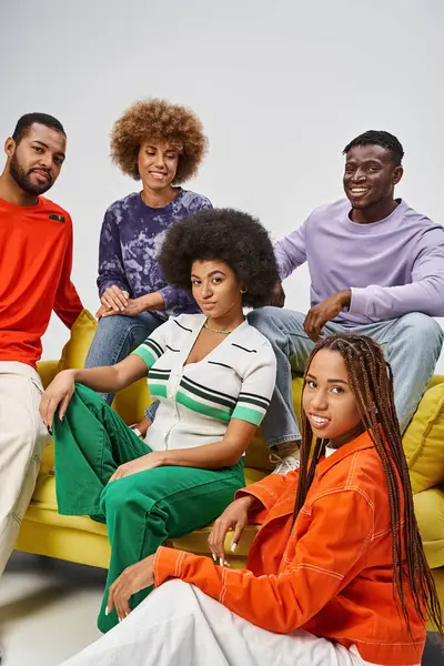 positive african american community in bright casual wear sitting together on yellow couch on grey