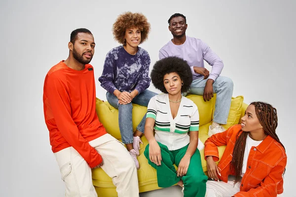 happy african american community in bright casual wear sitting together on yellow couch on grey