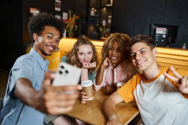 cheerful african american man taking selfie with stylish multiethnic friends in lounge of hostel clipart