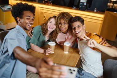 happy african american man taking selfie with trendy multiethnic students in hostel cafe, friendship clipart