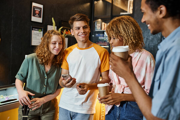 trendy man with smartphone near joyful multicultural friends at reception in modern hostel
