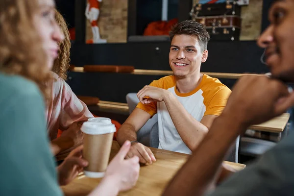 stock image blurred woman with paper cup talking to multiethnic friends in lounge cafe of hostel, fun and travel