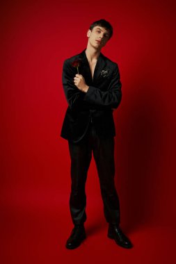 Rose 'u elinde tutan ve kırmızı arka plandaki kameraya bakan romantik bir adam. Çiçek.