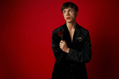 portrait of romantic young man holding rose in hand and looking away on red background, flower clipart