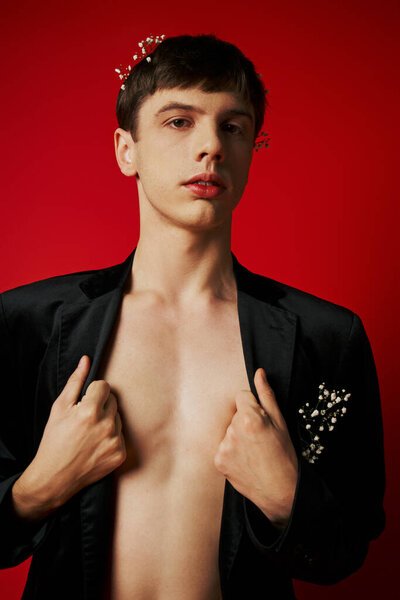 young man in velvet blazer with flowers in hair looking at camera and posing on red backdrop