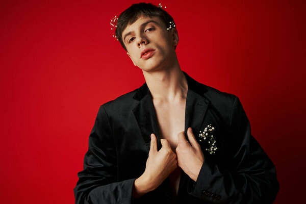 full length of young man with flowers in hair looking at camera and standing on red background