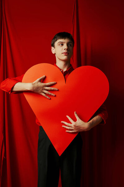 tall young man in black shorts embracing large heart cutout on red background, Valentines day