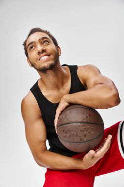 Gri arka planda basketbolla poz veren Afro-Amerikan spor giyimli çekici adam.