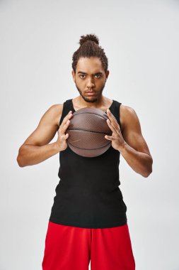 Güzel görünümlü Afro-Amerikan üniformalı adam basketbol topu tutuyor ve kameraya bakıyor.