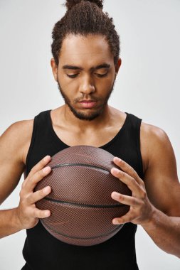 Çekici Afro-Amerikan üniformalı adam basketbol topuyla gri arka planda poz veriyor.
