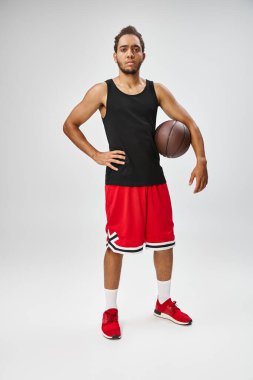 Basketbol oynayan yakışıklı Afro-Amerikan sporcu gri arka plandaki kameraya bakıyor.