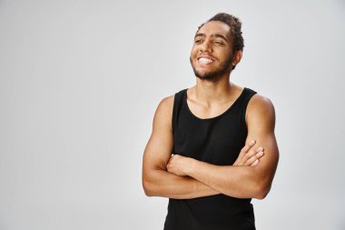 Neşeli, yakışıklı, Afro-Amerikan spor elbiseli adam gri arka planda kollarını kavuşturmuş poz veriyor.