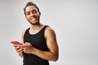 Neşeli atletik Afrikalı Amerikalı adam akıllı telefon tutuyor ve kameraya gülümsüyor, online bahis oynuyor.