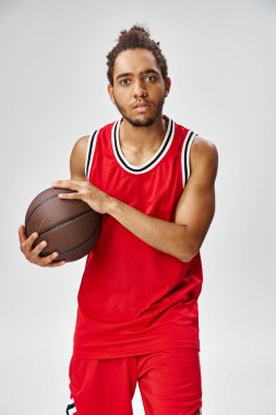 Spor giyimli yakışıklı Afro-Amerikan adam basketbol topu tutuyor ve kameraya bakıyor.