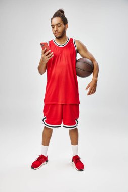 Yakışıklı Afro-Amerikalı adam elinde basketbolla akıllı telefonuna bakıyor.