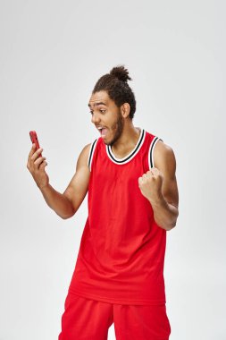 Mutlu afro-amerikan adam spor giyim sektöründe tezahürat yapıyor ve akıllı telefona bakıyor, online bahis oynuyor.