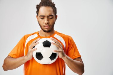 İyi görünümlü Afro-Amerikan sporcu rahat spor giyimli adam elinde futbola bakıyor.
