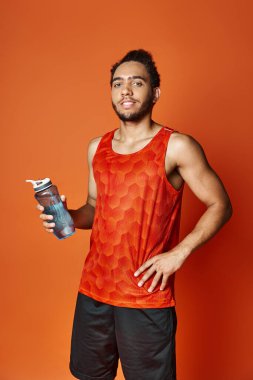 Çekici Afrikalı Amerikalı spor elbiseli adam elinde su şişesiyle kameraya bakıyor.