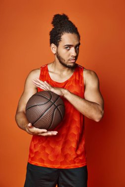 Güzel görünümlü Afro-Amerikan spor elbiseli adam basketbol topunu tutuyor ve kameraya bakıyor.