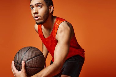 Turuncu arka planda basketbol oynayan canlı üniformalı Afro-Amerikalı çekici bir adam.