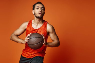 Çekici Afro-Amerikan spor giyimli adam turuncu arka planda aktif basketbol oynuyor.