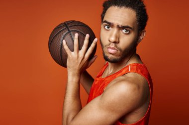 Yakışıklı Afro-Amerikalı canlı spor kıyafetleri içinde basketbol oynuyor ve kameraya bakıyor.