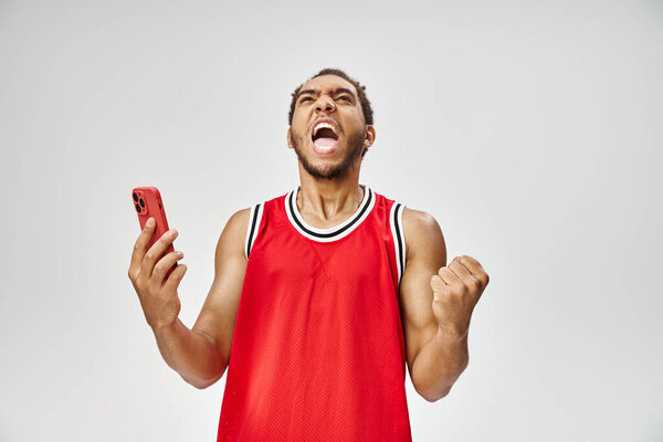 emotional handsome african american man holding smartphone on gray backdrop, online betting