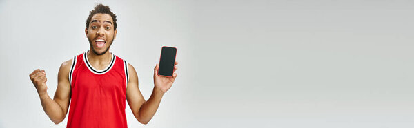 joyous african american man in sportwear holding phone and looking at camera, online betting, banner
