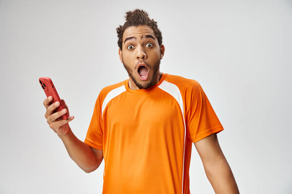 shocked african american man in sportwear holding phone and looking at camera, online betting