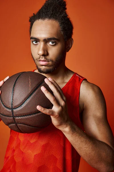 Çekici Afro-Amerikan spor elbiseli adam basketbol topunu tutuyor ve kameraya bakıyor.